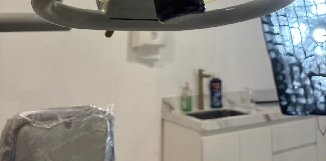 Sala de atendimento com bancada branca, cuba, torneira dourada, negatoscópio ligado e a cadeira ainda embalada