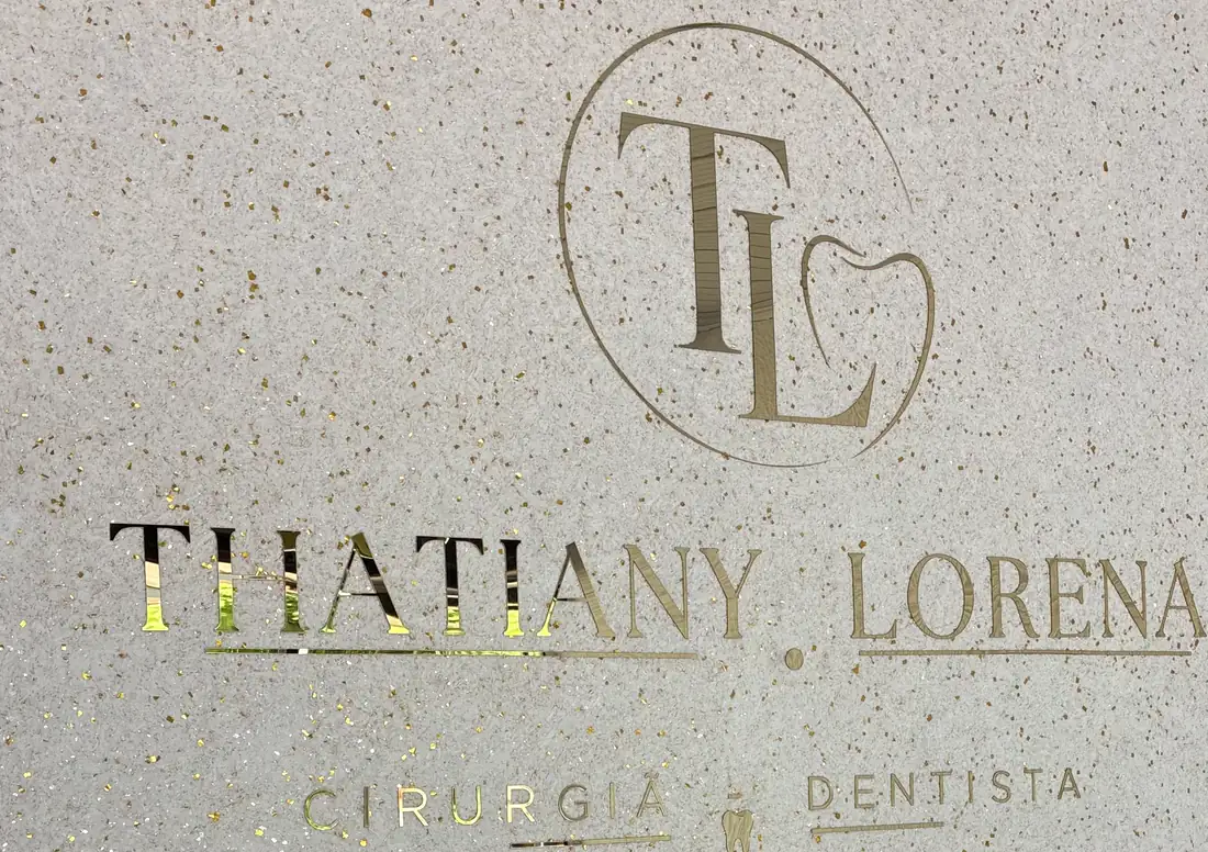 O nome Thatiany Lorena, Cirurgiã-Dentista, gravado em dourado na parede de concreto da recepção